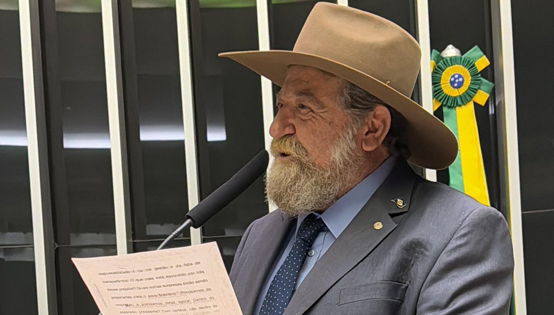 Nelson Barbudo, de chapéu e barba branca, discursa na tribuna da Câmara dos Deputados com a bandeira do Brasil ao fundo